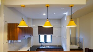A modern kitchen with wooden cabinets, a black countertop, and three yellow pendant lights. - Grand Plaza Inn (Tirur)