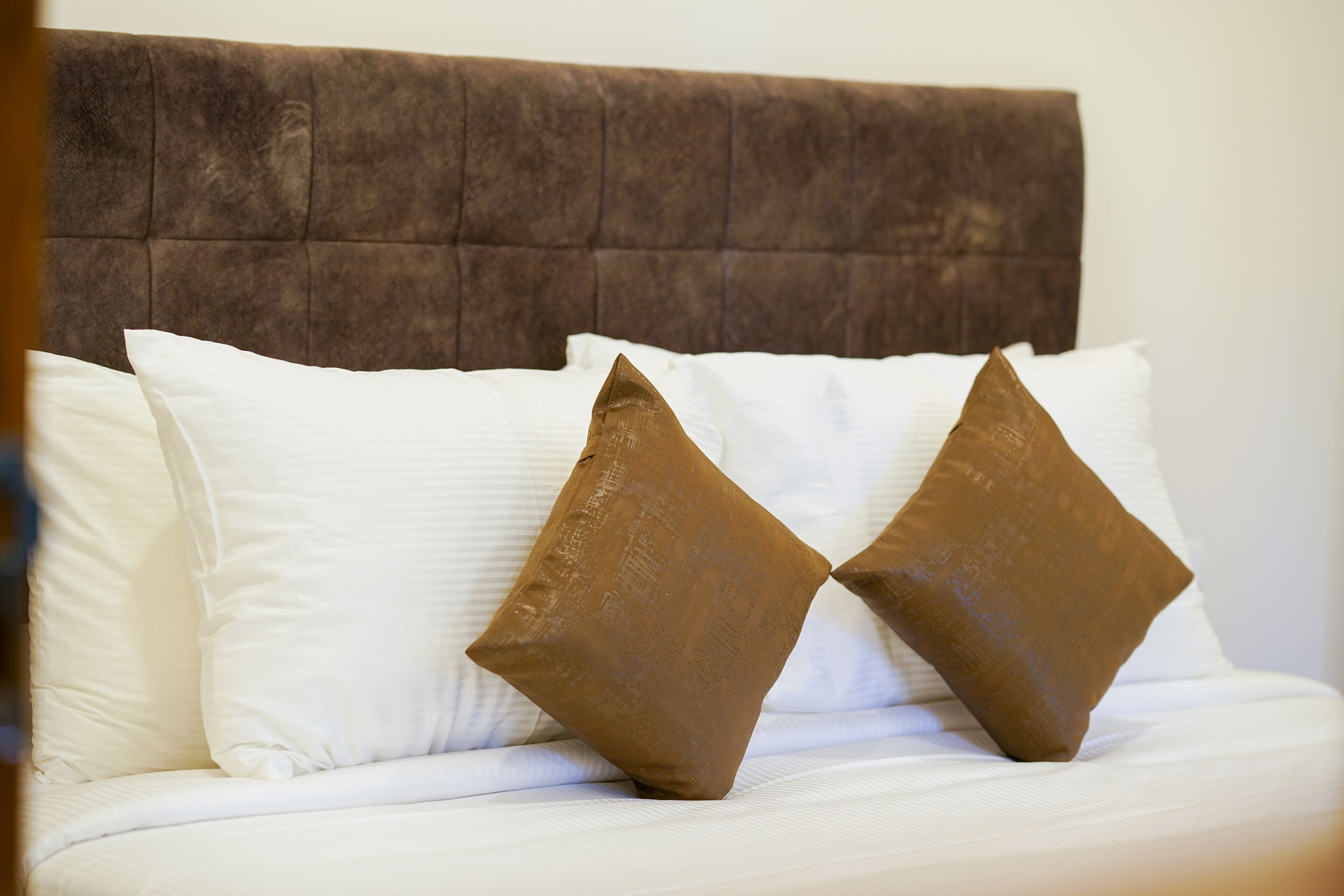 Cama com cabeceira estofada e dois travesseiros, um branco e um marrom.