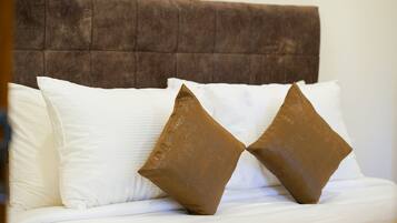 Cama com cabeceira estofada e dois travesseiros, um branco e um marrom.