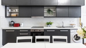 Una cocina moderna con armarios oscuros, encimeras blancas, horno empotrado y lavadora.