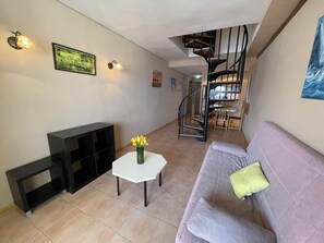 A living room with a sofa, a coffee table, a TV stand, a staircase, and a dining area.