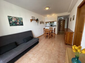 A living room with a sofa, dining table, chairs, a kitchen area, and a hallway leading to another room.