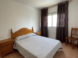A bedroom with a wooden bed, a nightstand, a chair, and a window with curtains.