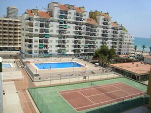 A multi-story hotel with balconies, a swimming pool, and a tennis court.