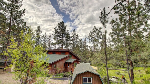 A rustic cabin with a large front porch, surrounded by tall pine trees and a clear sky. - Peaceful and spacious home tucked away at the base of the Mission Mountains. (St. Ignatius)