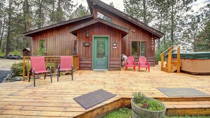 A wooden cabin with a green door, a deck with red chairs, and a hot tub. - Peaceful and spacious home tucked away at the base of the Mission Mountains. (St. Ignatius)
