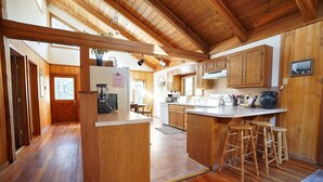 A wooden cabin kitchen with a central island, wooden bar stools, and a view of the outdoors. - Peaceful and spacious home tucked away at the base of the Mission Mountains. (St. Ignatius)