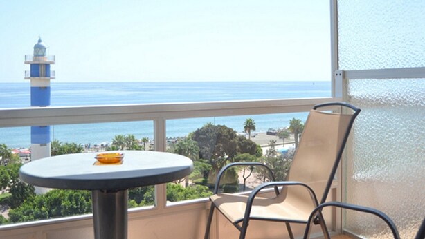 A balcony with a table and chairs, overlooking a beach and a lighthouse.