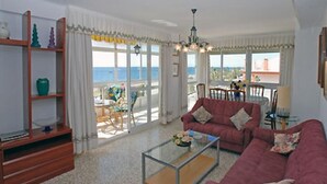 A living room with a red sofa, a glass coffee table, and a view of the sea through large windows.