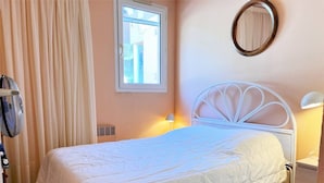 A bedroom with a bed, a window, a mirror, and a fan.