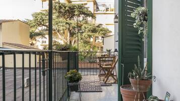 Un balcone con tavolo e sedie, piante in vaso e vista sugli edifici vicini.