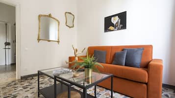 Un soggiorno con un tavolino in vetro, un divano arancione e un quadro appeso alla parete.