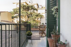 Un balcon avec une table et des chaises, des plantes en pot et une vue sur les bâtiments voisins.