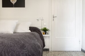 Une chambre à coucher avec un lit, une table de chevet avec une lampe, une porte et une petite plante accrochée au mur.