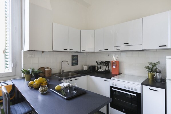 A modern kitchen with white cabinets, a black countertop, a stove, and a coffee machine. - Casa Gin Tonic, quiet house with terrace (Firenze)