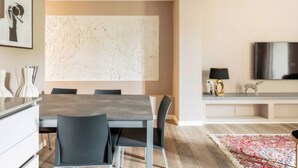 Un salon moderne comprenant un coin repas, une grande peinture abstraite au mur, un téléviseur à écran plat et un tapis à motifs.