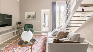Un salon moderne avec un canapé, un fauteuil vert, une table basse, un téléviseur et un escalier.
