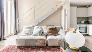Un salon moderne avec un canapé, un tapis à motifs et un escalier menant à un espace cuisine.