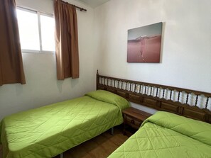 A room with two single beds, a wooden headboard, a small wooden nightstand, and a painting on the wall.