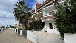 A residential street with white houses, palm trees, and a clear sky.