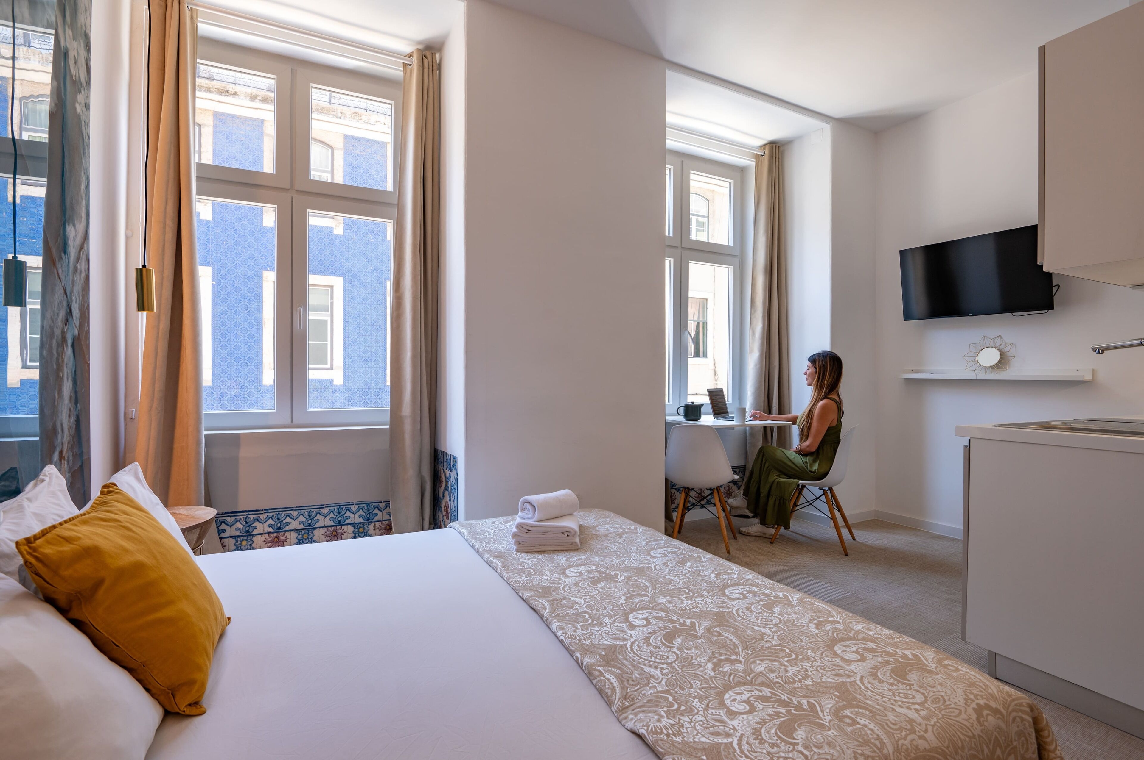 Una camera d'albergo con un letto, una scrivania, una sedia e una televisione a parete.