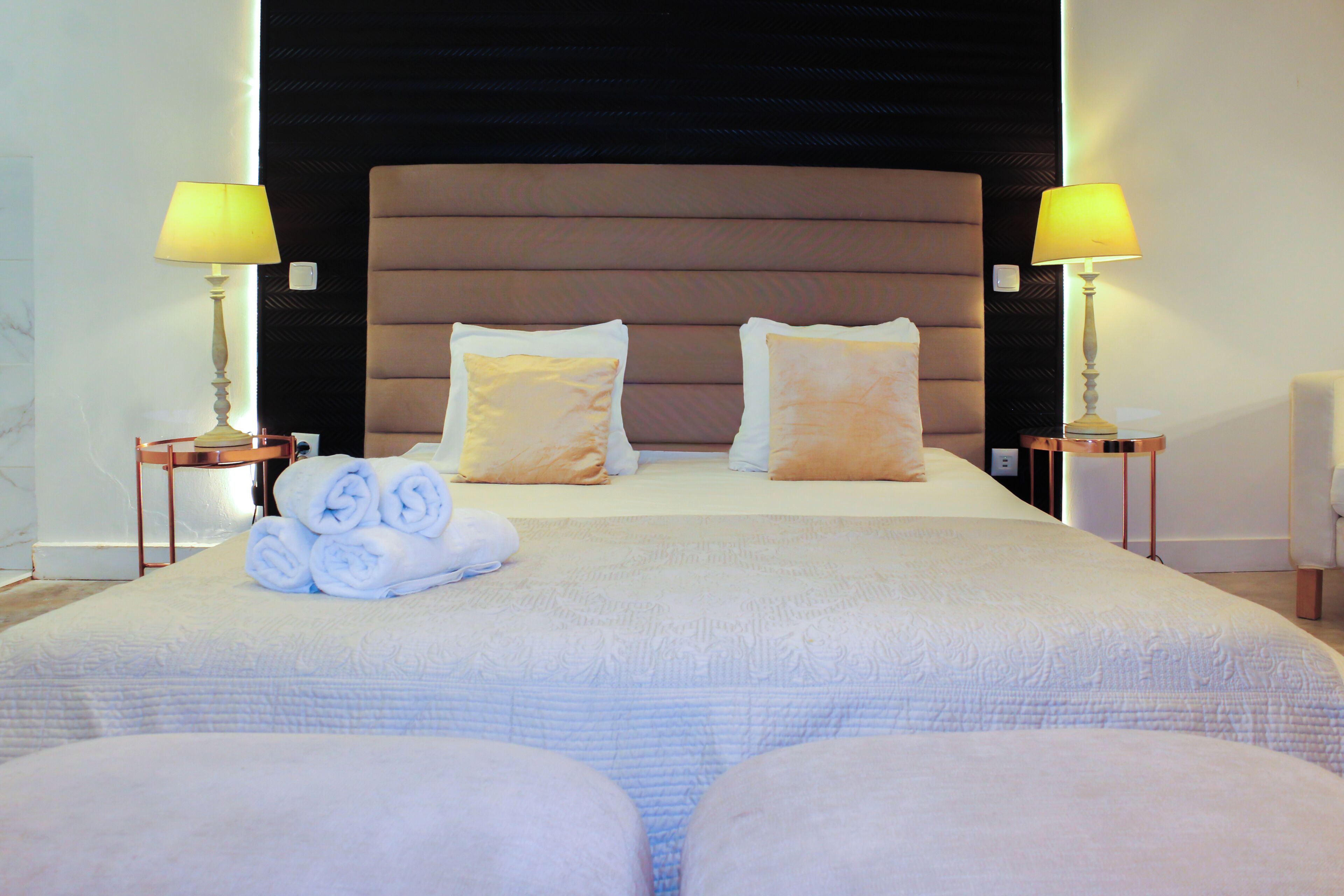 A neatly made bed with pillows, a stack of towels, and two bedside lamps.