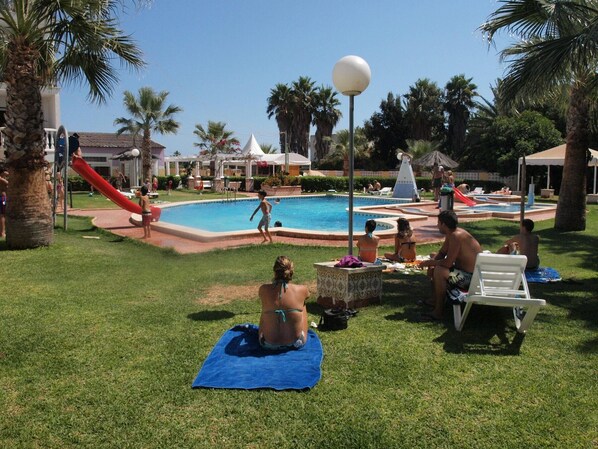 A pool area with a slide, palm trees, and people relaxing on towels.