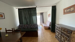 Ein Zimmer mit einem Holzes Esstisch, einer Couch, einem Schrank mit Schubladen und einem gemusterten Kissen auf der Couch.
