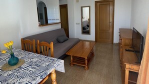 A living room with a sofa, a dining table with chairs, a TV stand, and a mirror. - Cozy 2-Bed Apartment, 150m from Beach, Pool, Parking, Peníscola (Peñíscola)