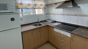 A kitchen with a microwave, stove, sink, and wooden cabinets. - Cozy 2-Bed Apartment, 150m from Beach, Pool, Parking, Peníscola (Peñíscola)