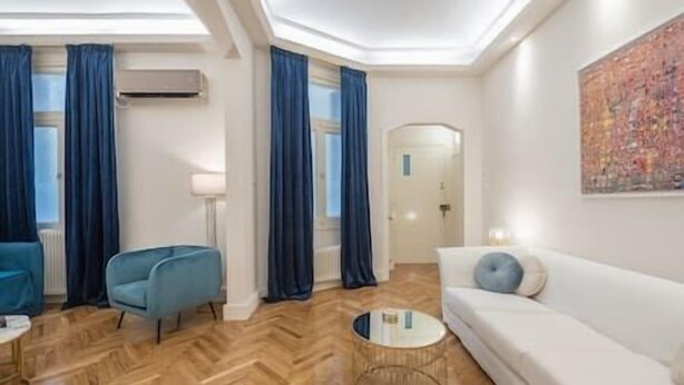 A modern living room with a herringbone wood floor, a white sofa, a blue armchair, and a round coffee table. - Kolonaki Private Garden (Athina)