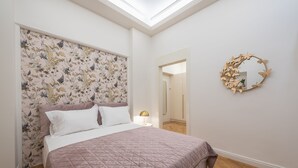 A bedroom with a bed, floral wallpaper, a round mirror, and a skylight. - Kolonaki Private Garden (Athina)