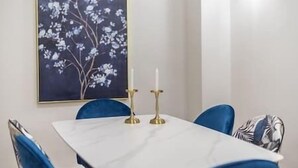 A dining area with a white table, blue chairs, and a floral painting on the wall. - Kolonaki Private Garden (Athina)