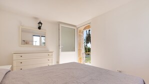 Een slaapkamer met een groot bed, een dressoir, een spiegel en een deur die naar een buitenruimte leidt.