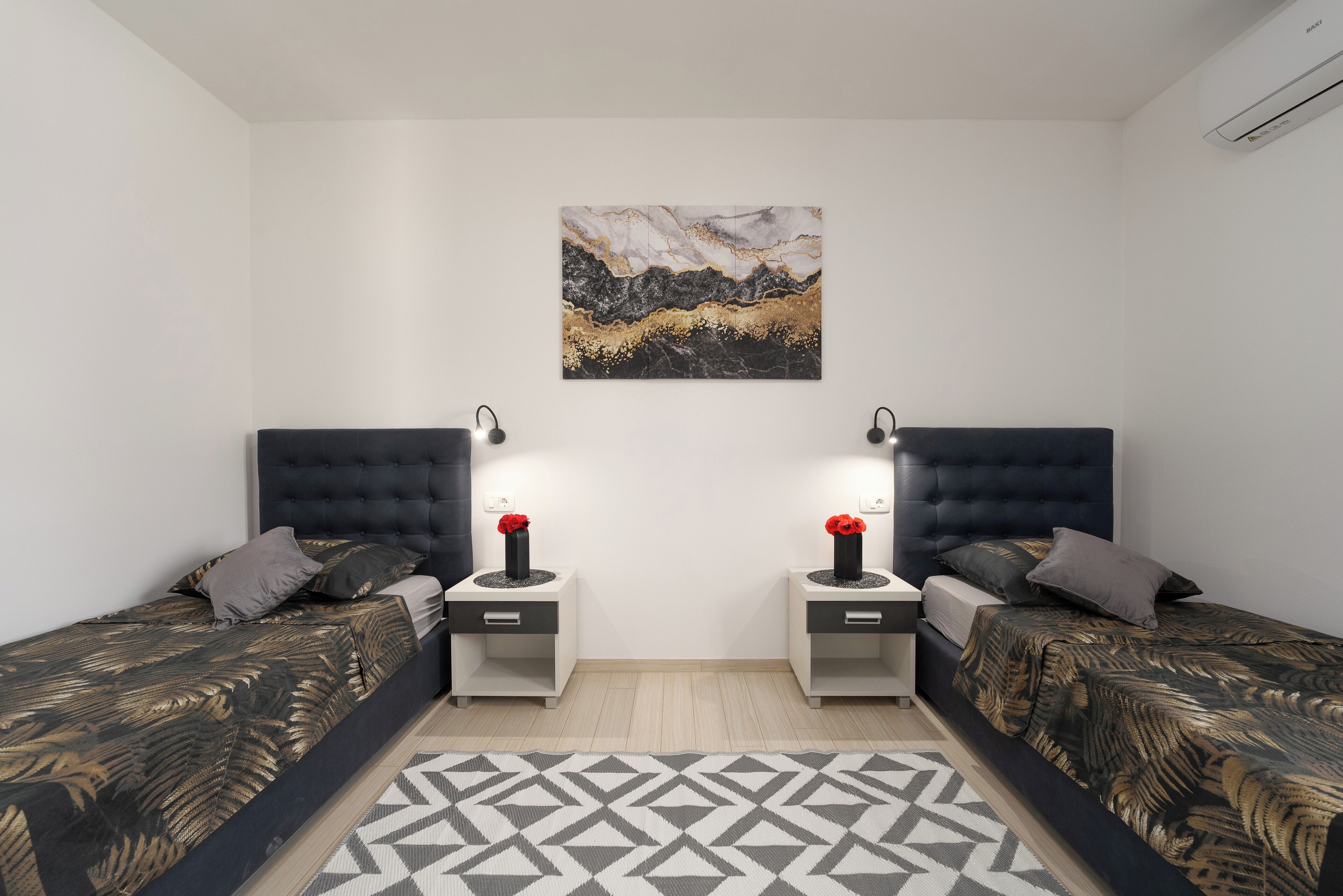 Una camera da letto moderna con due letti, un tappeto geometrico e un quadro appeso al muro.