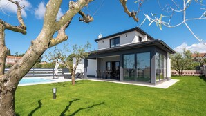 Una casa moderna con un amplio ventanal, una piscina y un césped bien cuidado.