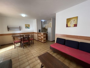 A compact living space with a kitchenette, a dining area with wooden furniture, and a sofa with cushions.