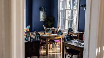 Un comedor con mesas y sillas de madera, un ventanal grande y una planta en maceta.