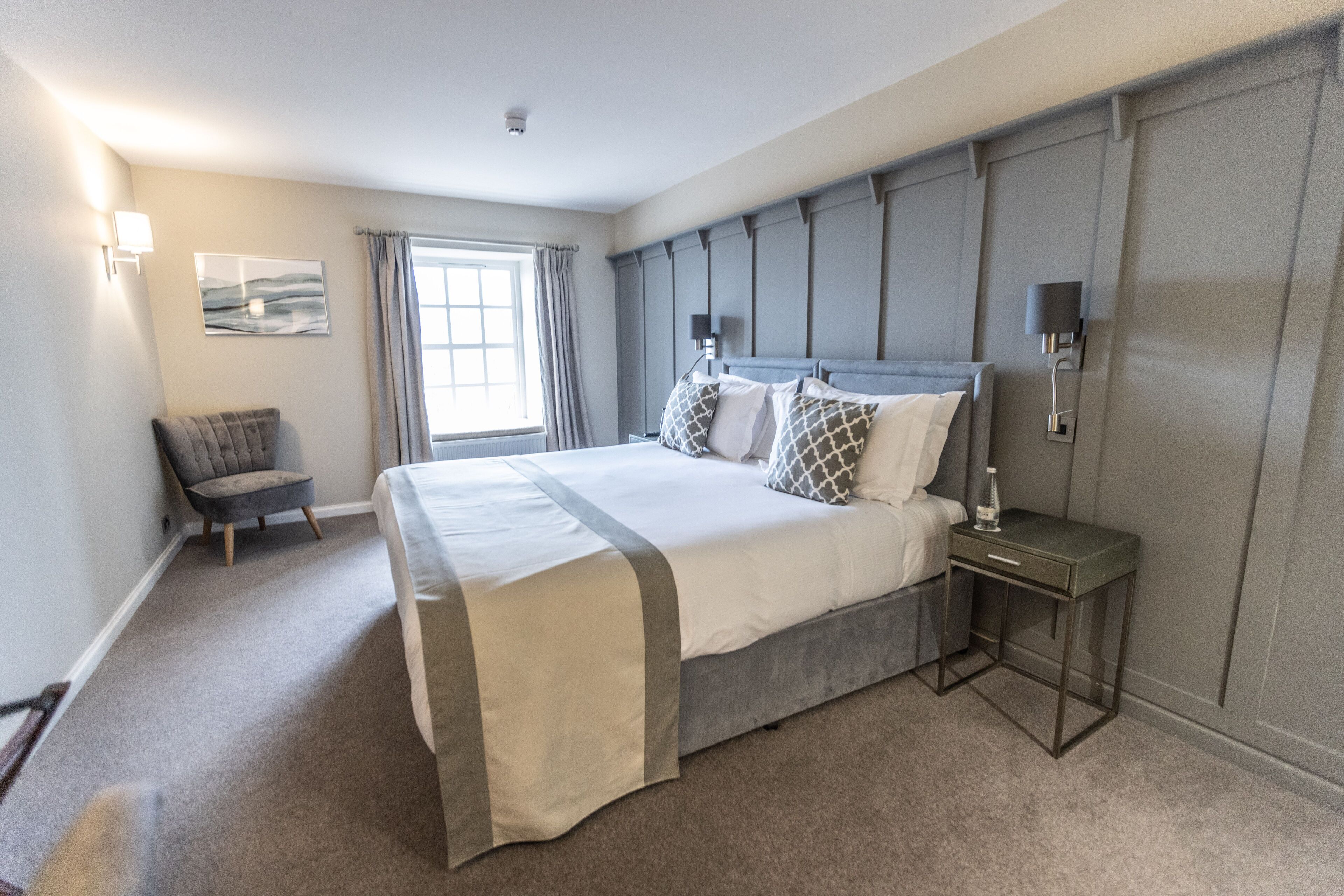 Une chambre moderne avec un grand lit, une table de chevet, une chaise et une fenêtre avec des rideaux.