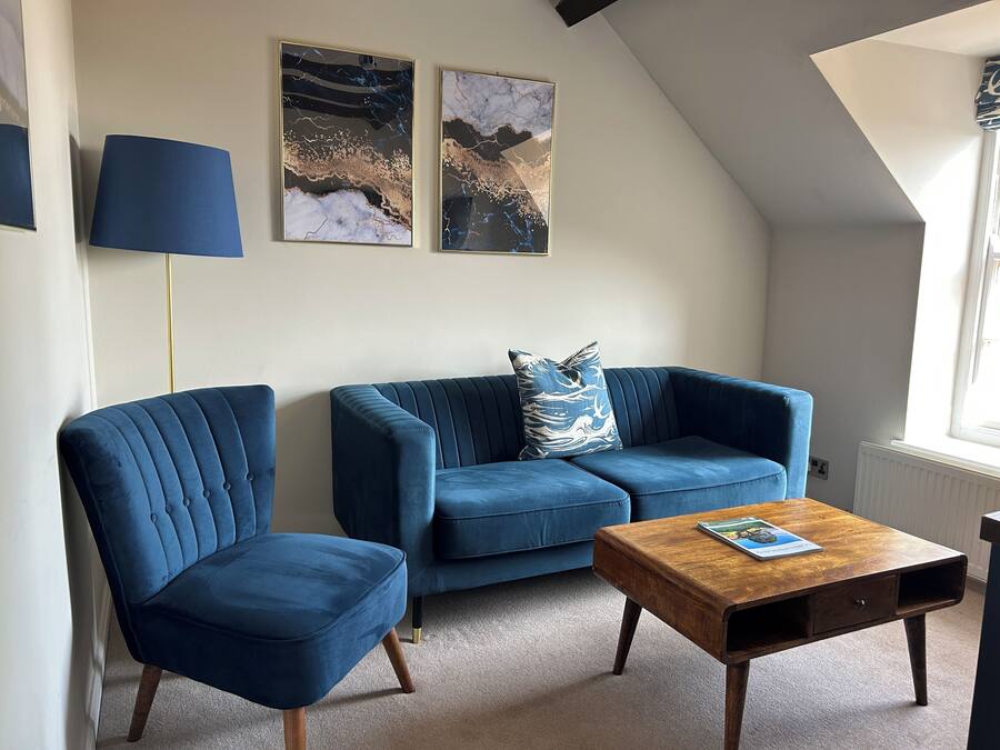 Un salon moderne avec un canapé bleu, un fauteuil assorti et une table basse en bois. Deux tableaux abstraits ornent le mur, et une lampe sur pied est placée dans un coin.