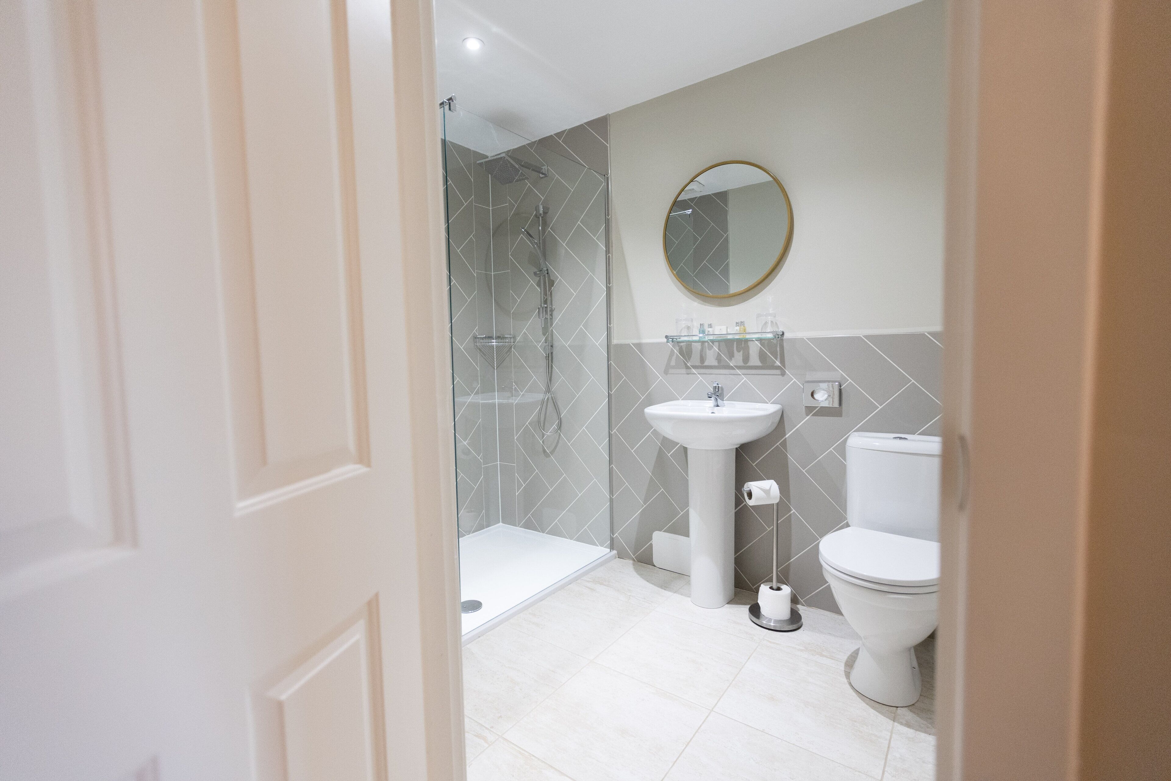 Un baño moderno con cabina de ducha de vidrio, lavamanos pedestal y retrete.