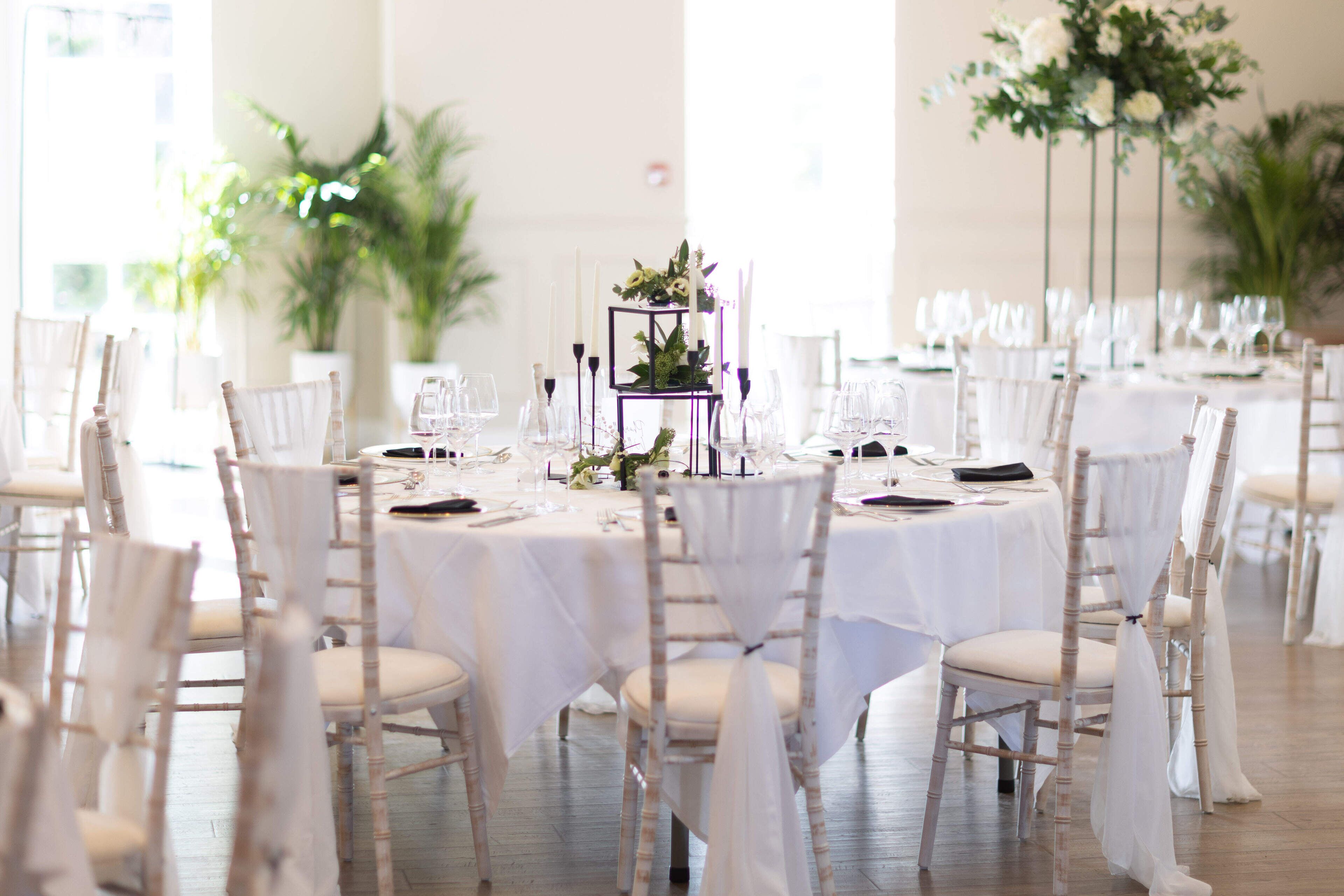Un salón de banquetes con mesas redondas, manteles blancos y sillas cubiertas de blanco.