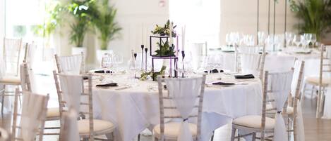 Un salón de banquetes con mesas redondas, manteles blancos y sillas cubiertas de blanco.