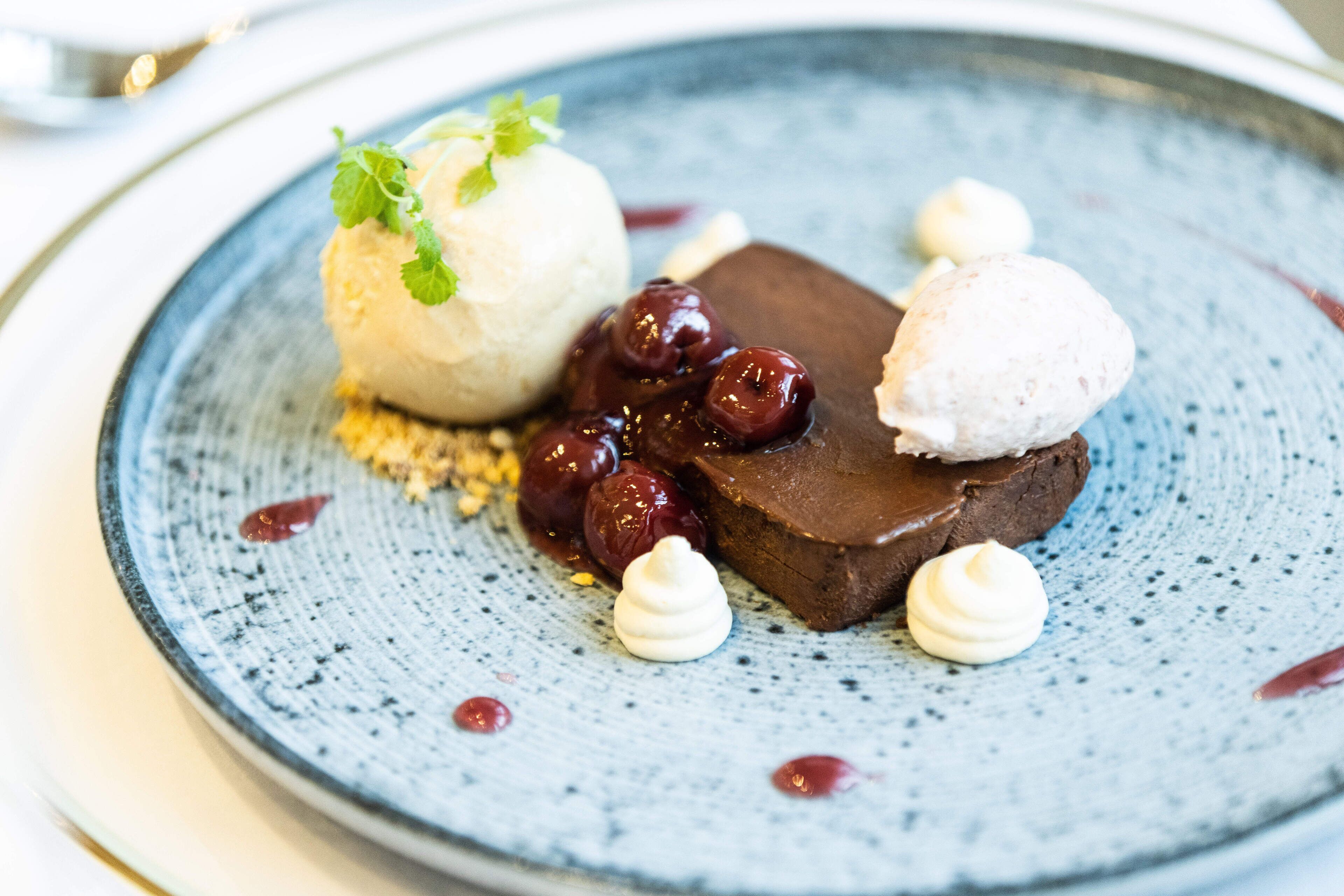 A dessert plate with a chocolate dessert, cherries, and a scoop of ice cream.