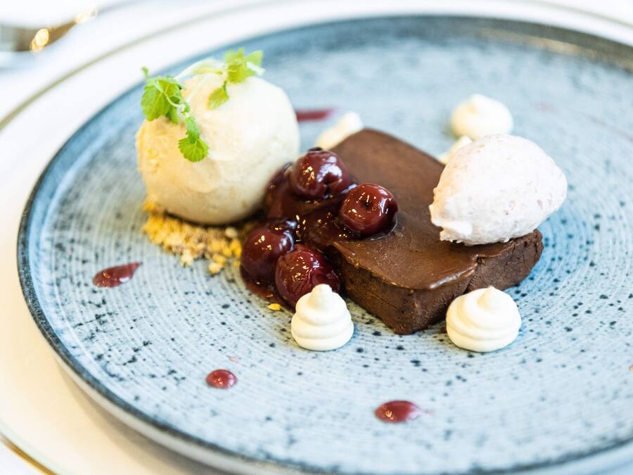 A dessert plate with a chocolate dessert, cherries, and a scoop of ice cream.