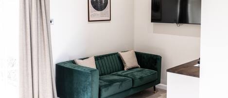 Ein Zimmer mit einem grünen Samsofa, einem gerahmten Bild an der Wand und einem flachbildfernseher, der darüber angebracht ist.