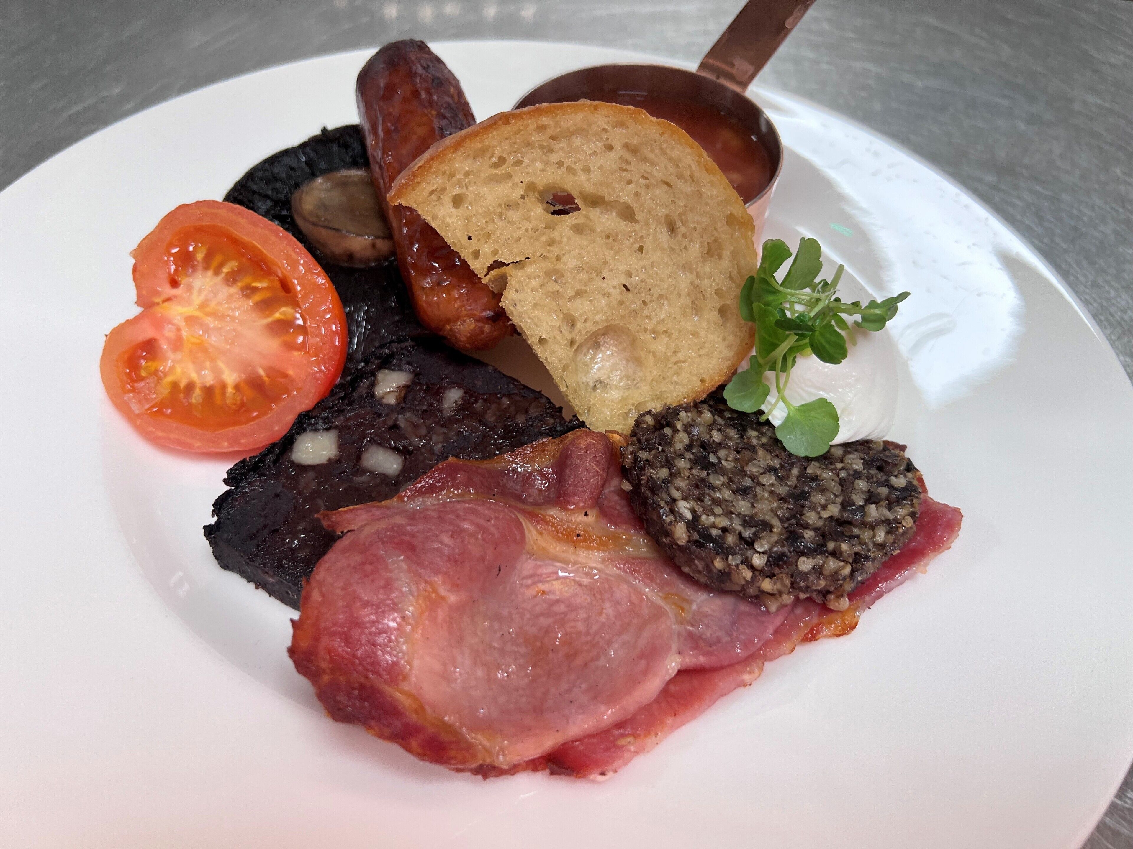 Une assiette contenant divers éléments pour le petit-déjeuner, notamment des saucisses, une tranche de pain, une tomate, un morceau de bacon et un champignon.