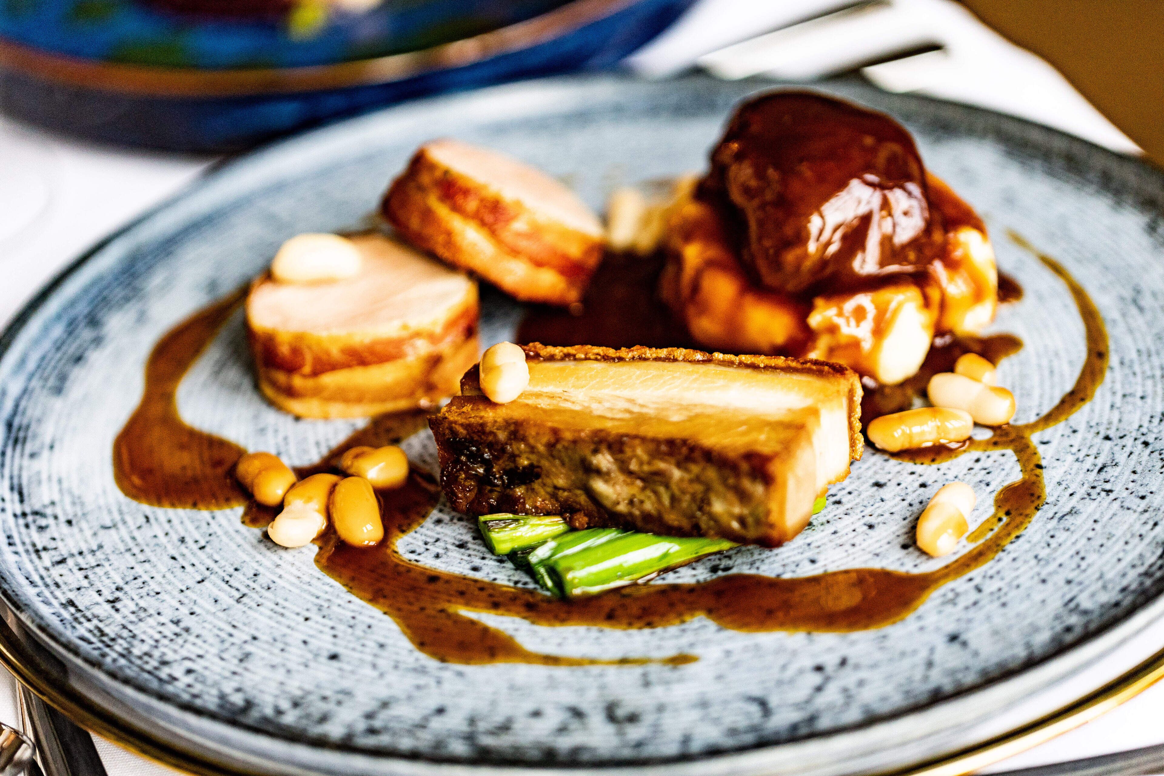 Une assiette contenant un morceau de viande, peut-être du porc, accompagné de légumes verts et de cacahuètes.