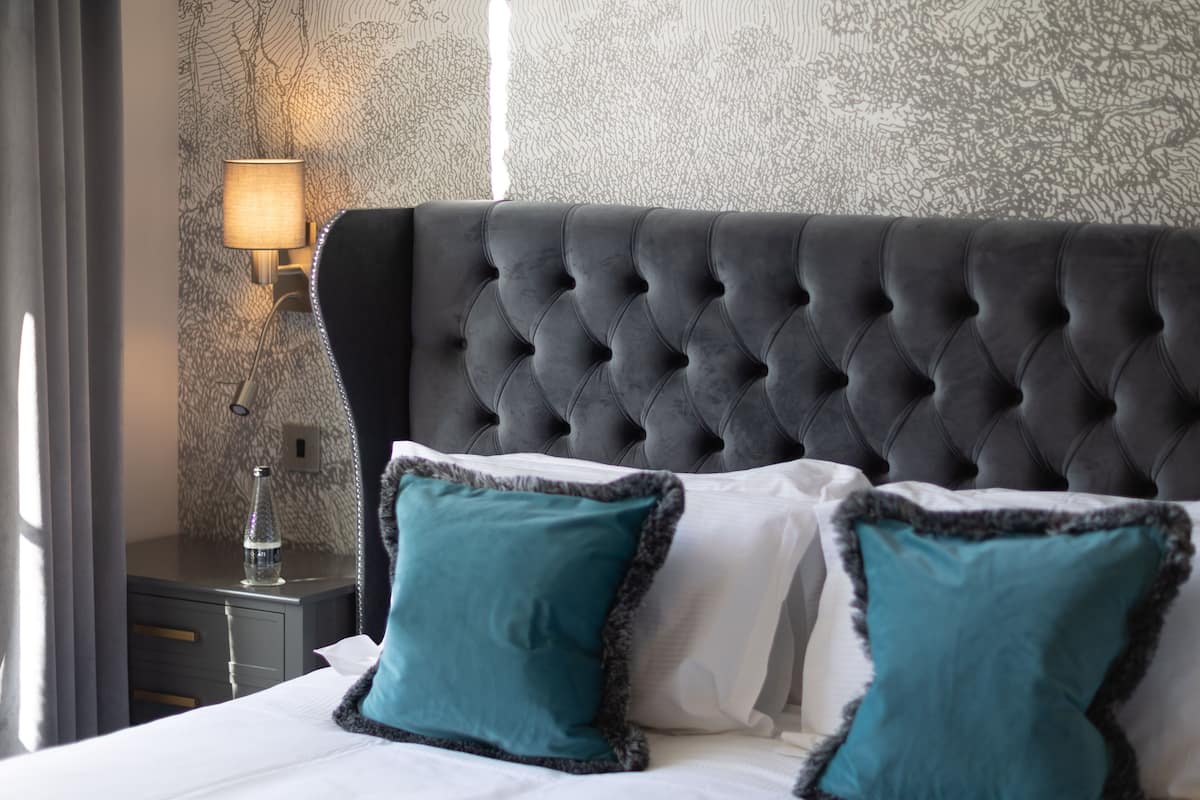A neatly made bed with a tufted headboard, two teal pillows, and a bedside lamp.