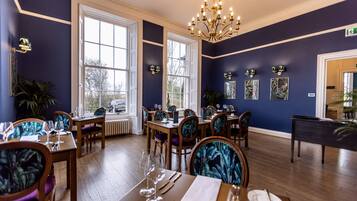 A dining area with tables set for service, large windows, and a chandelier.